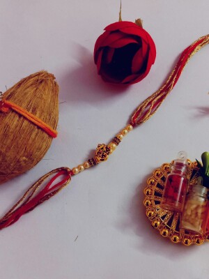 Red and yellow om rakhi for bhai complete with mini nariyal roli, and chawal